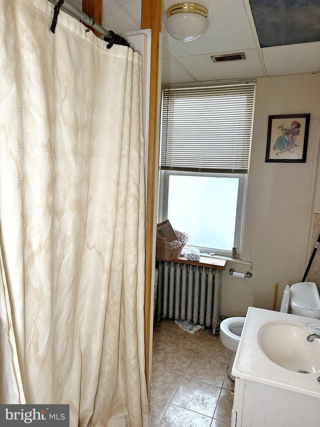 bathroom featuring a drop ceiling, radiator, vanity, tile patterned flooring, and toilet