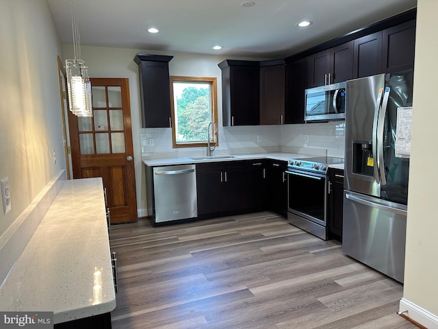 kitchen with appliances with stainless steel finishes, tasteful backsplash, sink, light wood-type flooring, and light stone countertops