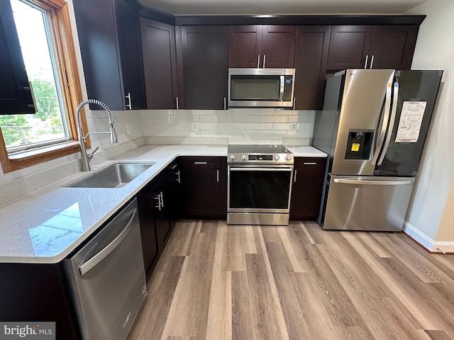 kitchen with appliances with stainless steel finishes, light hardwood / wood-style flooring, sink, backsplash, and light stone countertops