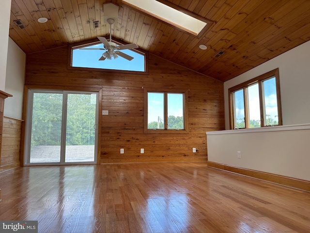 interior space with wooden walls, ceiling fan, light hardwood / wood-style flooring, and a skylight