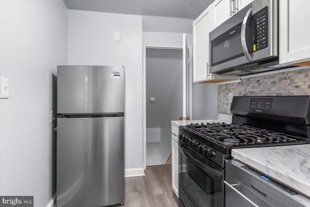 kitchen with light stone counters, backsplash, appliances with stainless steel finishes, white cabinets, and light wood-type flooring