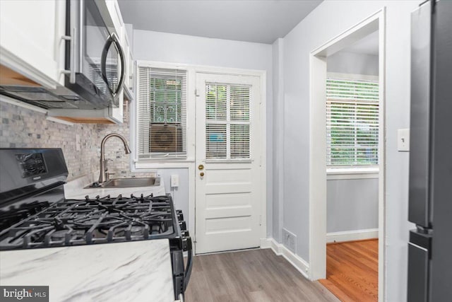 kitchen featuring sink, decorative backsplash, light stone countertops, light hardwood / wood-style floors, and black range with gas cooktop