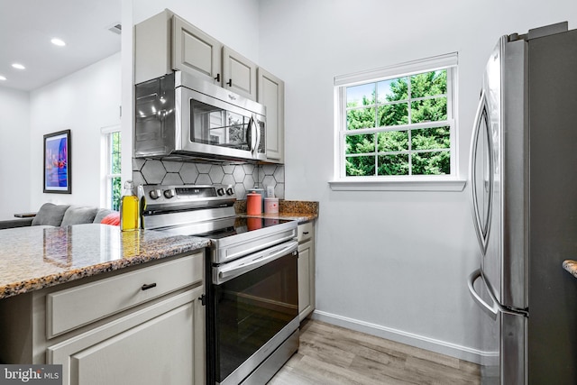 kitchen featuring stainless steel appliances, light hardwood / wood-style flooring, backsplash, dark stone countertops, and gray cabinets