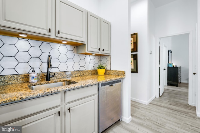 kitchen featuring white cabinetry, sink, light stone counters, stainless steel dishwasher, and backsplash