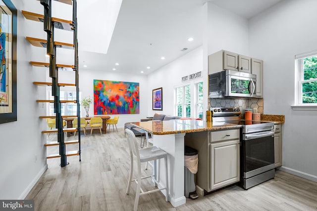 kitchen with gray cabinets, a kitchen bar, light wood-type flooring, and appliances with stainless steel finishes