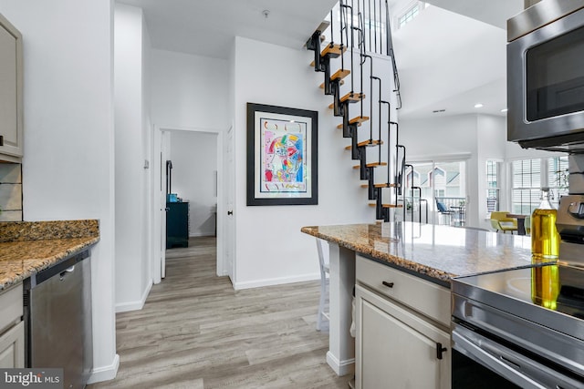 kitchen with white cabinets, light wood-type flooring, light stone countertops, and stainless steel appliances