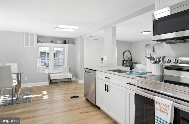 kitchen featuring appliances with stainless steel finishes, light wood-type flooring, white cabinetry, and sink