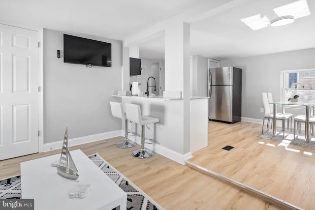 kitchen with kitchen peninsula, stainless steel fridge, light hardwood / wood-style floors, and sink