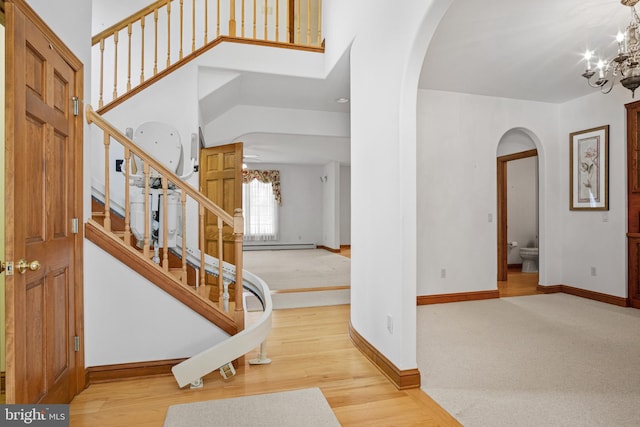 entryway with a high ceiling, wood-type flooring, a baseboard heating unit, and an inviting chandelier