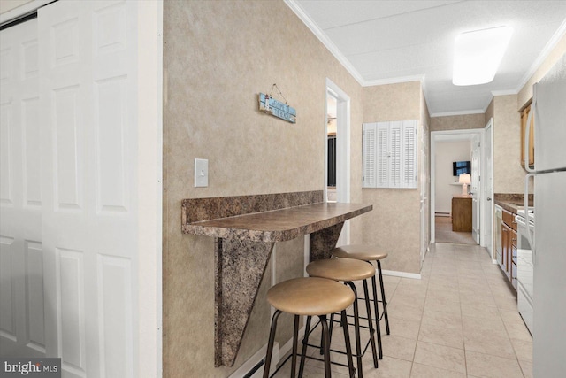 kitchen featuring electric range, light tile patterned flooring, a kitchen bar, and crown molding