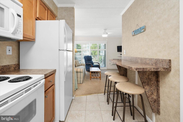 kitchen with a kitchen breakfast bar, white appliances, light tile patterned floors, and ornamental molding