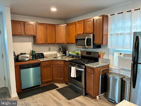 kitchen featuring light stone counters, stainless steel appliances, light hardwood / wood-style flooring, and cooling unit