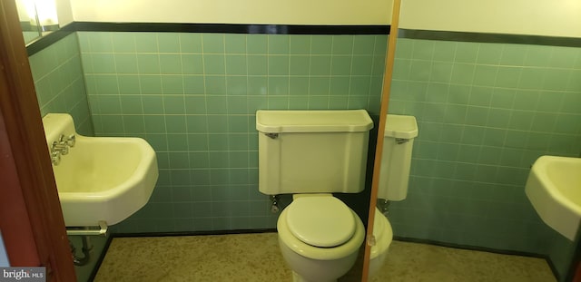 bathroom with toilet, sink, and tile walls