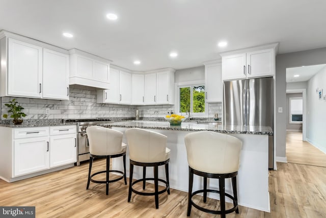 kitchen with a kitchen bar, dark stone counters, stainless steel appliances, light hardwood / wood-style flooring, and white cabinets