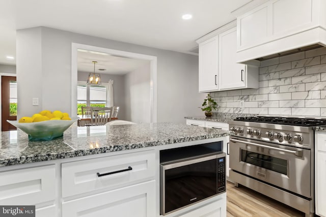 kitchen featuring stone counters, built in microwave, tasteful backsplash, high end stainless steel range, and white cabinets