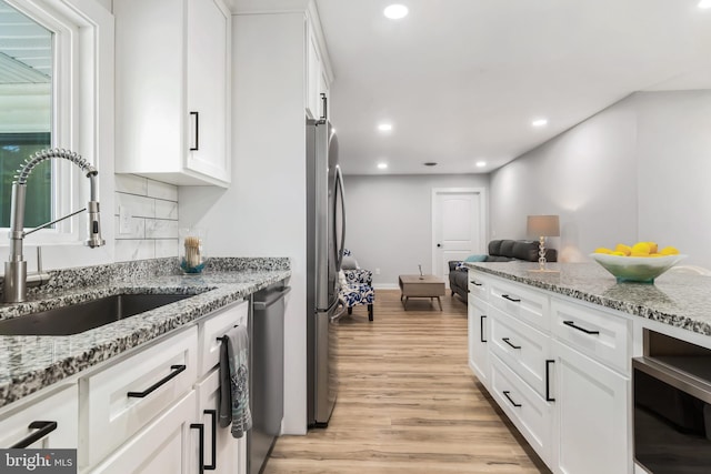 kitchen featuring light stone counters, stainless steel appliances, beverage cooler, sink, and white cabinets