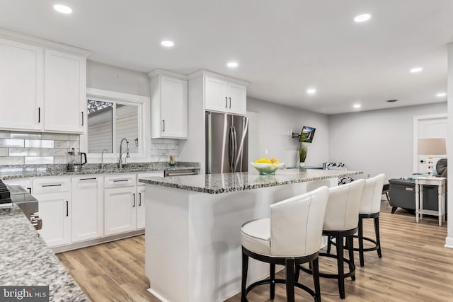 kitchen featuring light hardwood / wood-style floors, light stone counters, white cabinetry, and stainless steel refrigerator