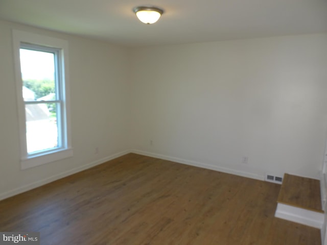 unfurnished room featuring baseboards, visible vents, and dark wood finished floors