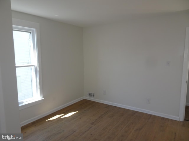 spare room with a healthy amount of sunlight, dark wood-style floors, baseboards, and visible vents