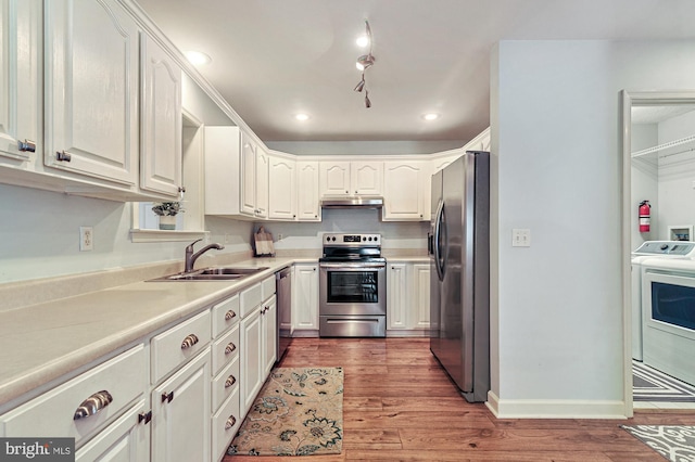 kitchen with appliances with stainless steel finishes, washer / clothes dryer, white cabinetry, and sink