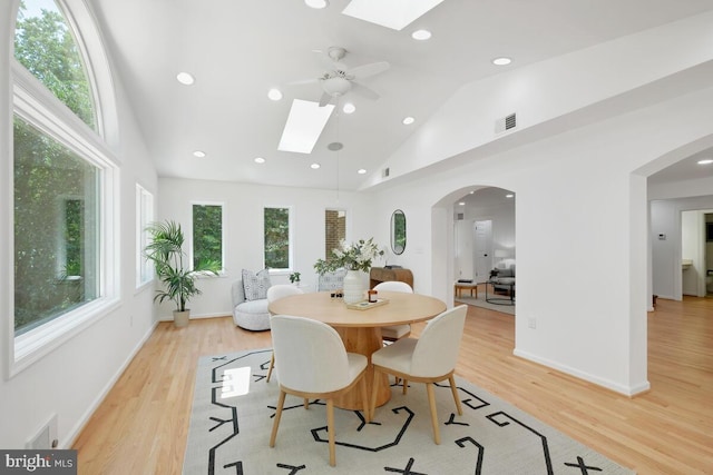 dining room with ceiling fan, a skylight, light hardwood / wood-style flooring, and high vaulted ceiling