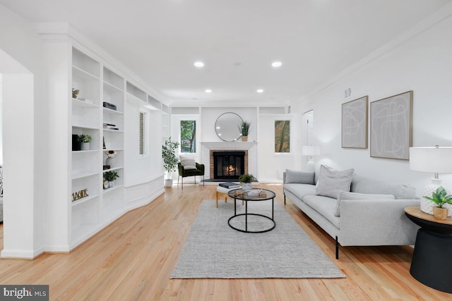 living room featuring built in shelves, light wood-type flooring, a fireplace, and ornamental molding