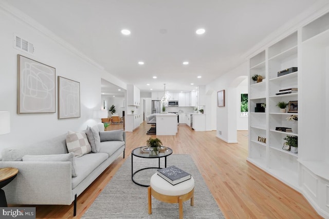 living room featuring built in features, light hardwood / wood-style flooring, and crown molding