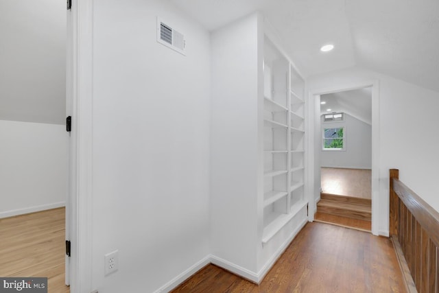 hallway with lofted ceiling, hardwood / wood-style floors, and built in shelves