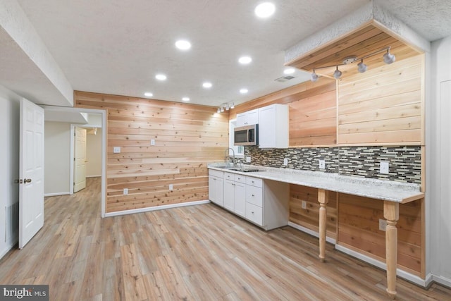 kitchen with light wood-type flooring, light stone counters, wood walls, and white cabinetry