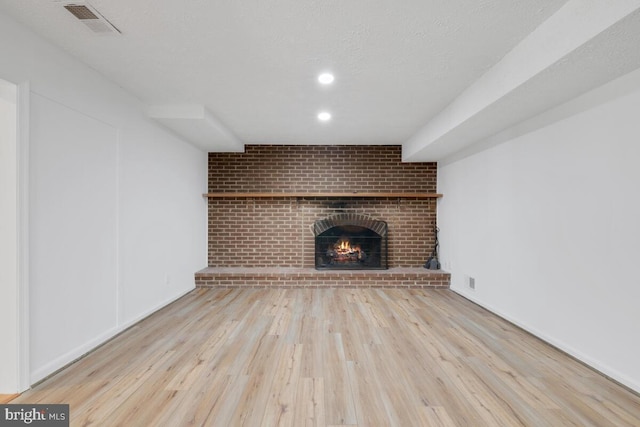 unfurnished living room featuring light wood-type flooring, a textured ceiling, and a fireplace