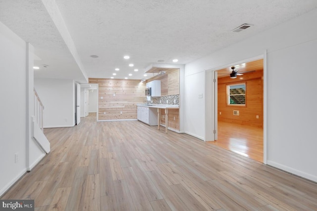 unfurnished living room with wood walls, a textured ceiling, and light hardwood / wood-style flooring