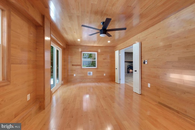 unfurnished room with wooden walls, wooden ceiling, a brick fireplace, ceiling fan, and light wood-type flooring