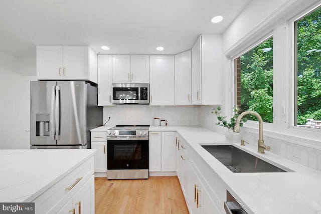 kitchen featuring light hardwood / wood-style floors, decorative backsplash, sink, white cabinetry, and stainless steel appliances