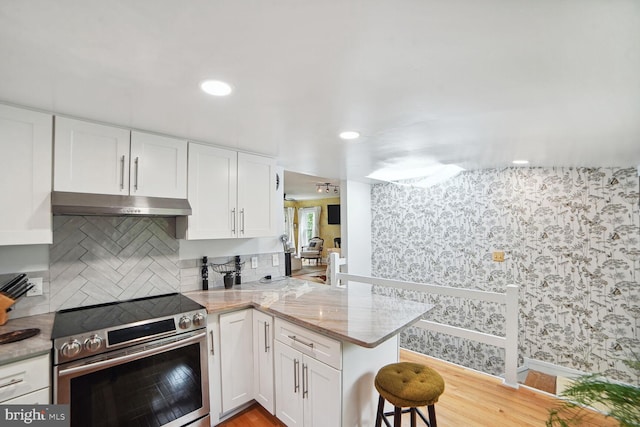 kitchen with electric range, a breakfast bar area, tasteful backsplash, kitchen peninsula, and white cabinets