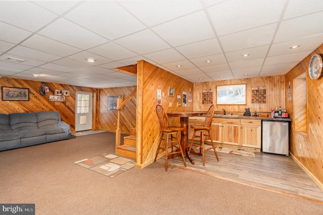 bar featuring a paneled ceiling, light hardwood / wood-style flooring, wooden walls, and stainless steel dishwasher