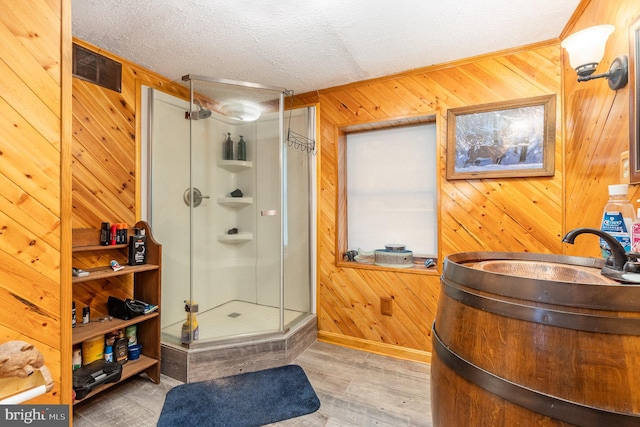 bathroom with a shower with door, hardwood / wood-style floors, sink, a textured ceiling, and wood walls