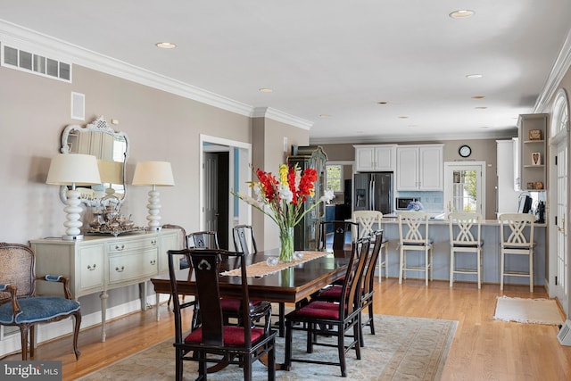 dining area with plenty of natural light, ornamental molding, and light hardwood / wood-style flooring