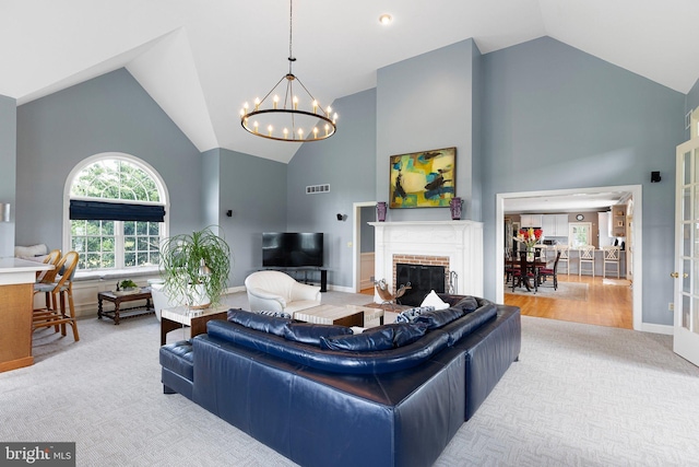 living room with high vaulted ceiling, light colored carpet, a brick fireplace, and a notable chandelier