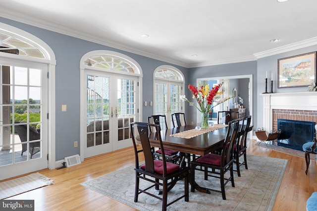 dining room featuring french doors, light hardwood / wood-style flooring, a brick fireplace, and ornamental molding