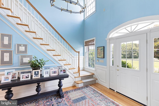 entrance foyer with a healthy amount of sunlight, an inviting chandelier, a towering ceiling, and light hardwood / wood-style flooring