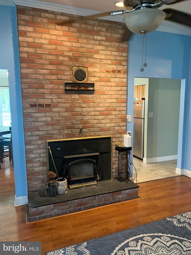 room details featuring a wood stove, crown molding, stainless steel refrigerator, ceiling fan, and wood-type flooring