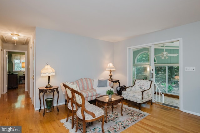 living area with attic access, wood finished floors, baseboards, and ceiling fan