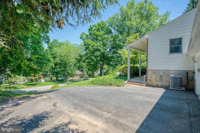 view of patio / terrace featuring central air condition unit, driveway, and view of wooded area