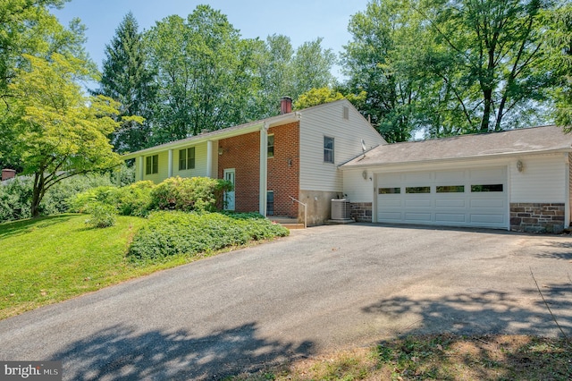 view of front facade with driveway, central AC unit, an attached garage, and stone siding