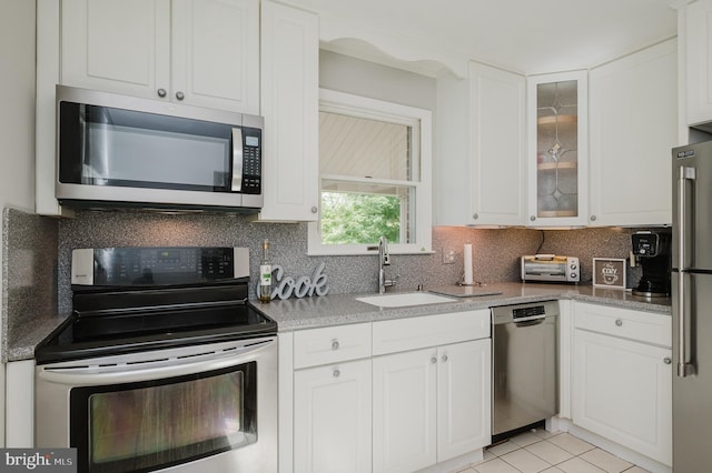 kitchen with stainless steel appliances, a sink, white cabinetry, glass insert cabinets, and tasteful backsplash