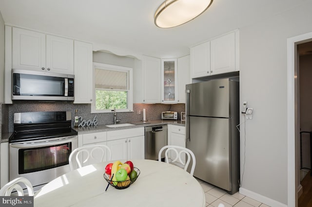 kitchen featuring stainless steel appliances, a sink, backsplash, glass insert cabinets, and white cabinetry
