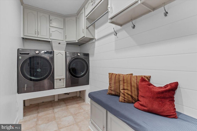 clothes washing area with wood walls, cabinets, and independent washer and dryer