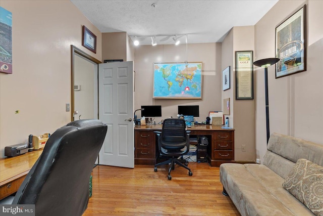 home office featuring a textured ceiling, rail lighting, and light hardwood / wood-style floors