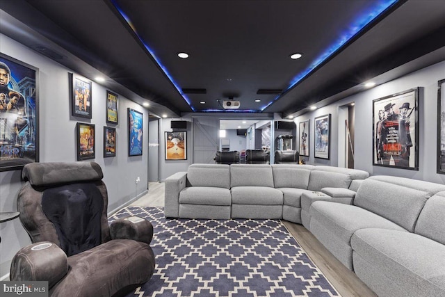 cinema room with a tray ceiling and light wood-type flooring