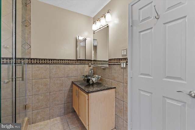 bathroom featuring tile patterned floors, a textured ceiling, tiled shower, vanity, and tile walls